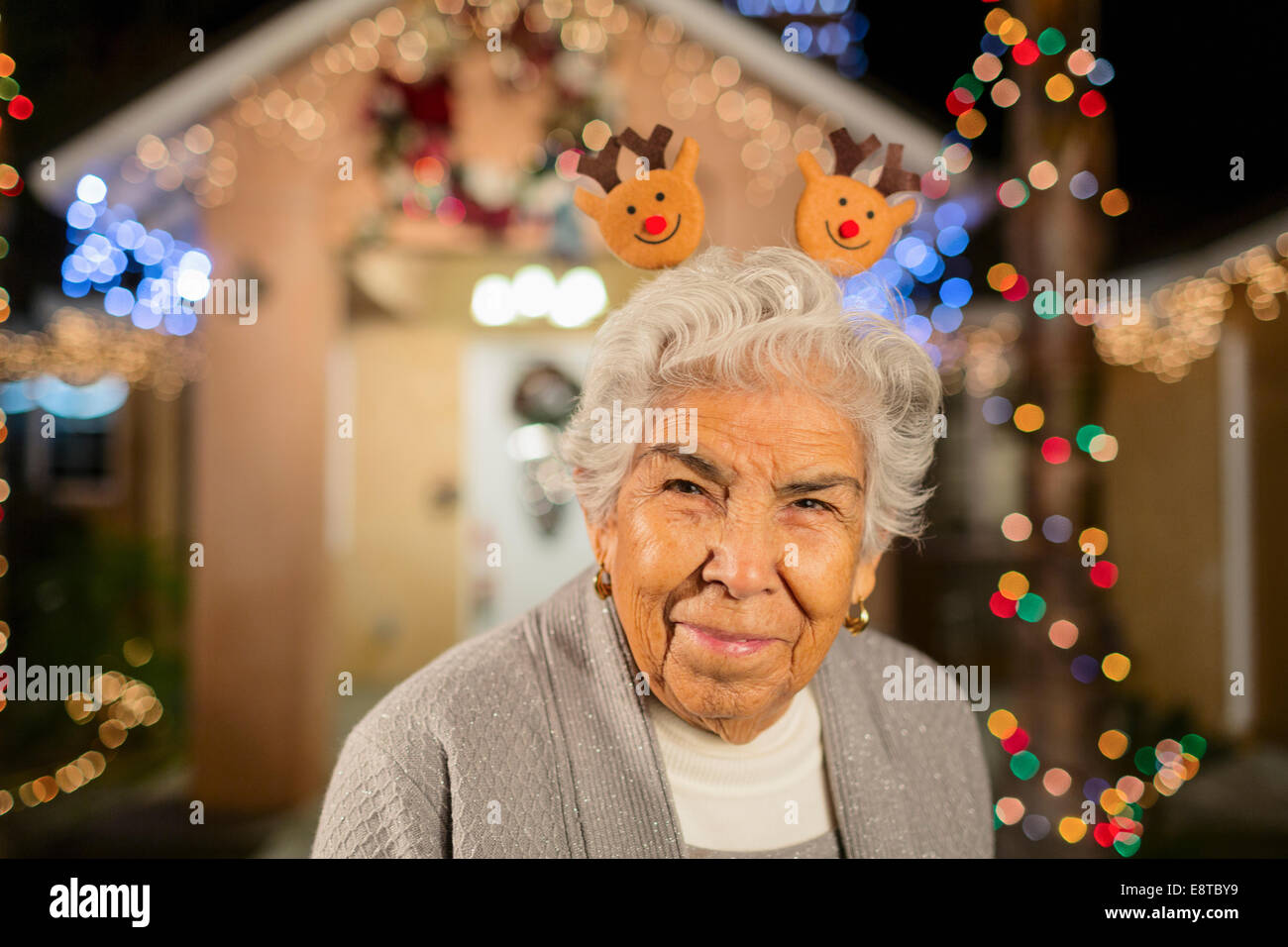Ältere Hispanic Frau lächelnd vor Haus mit Lichterketten dekoriert Stockfoto