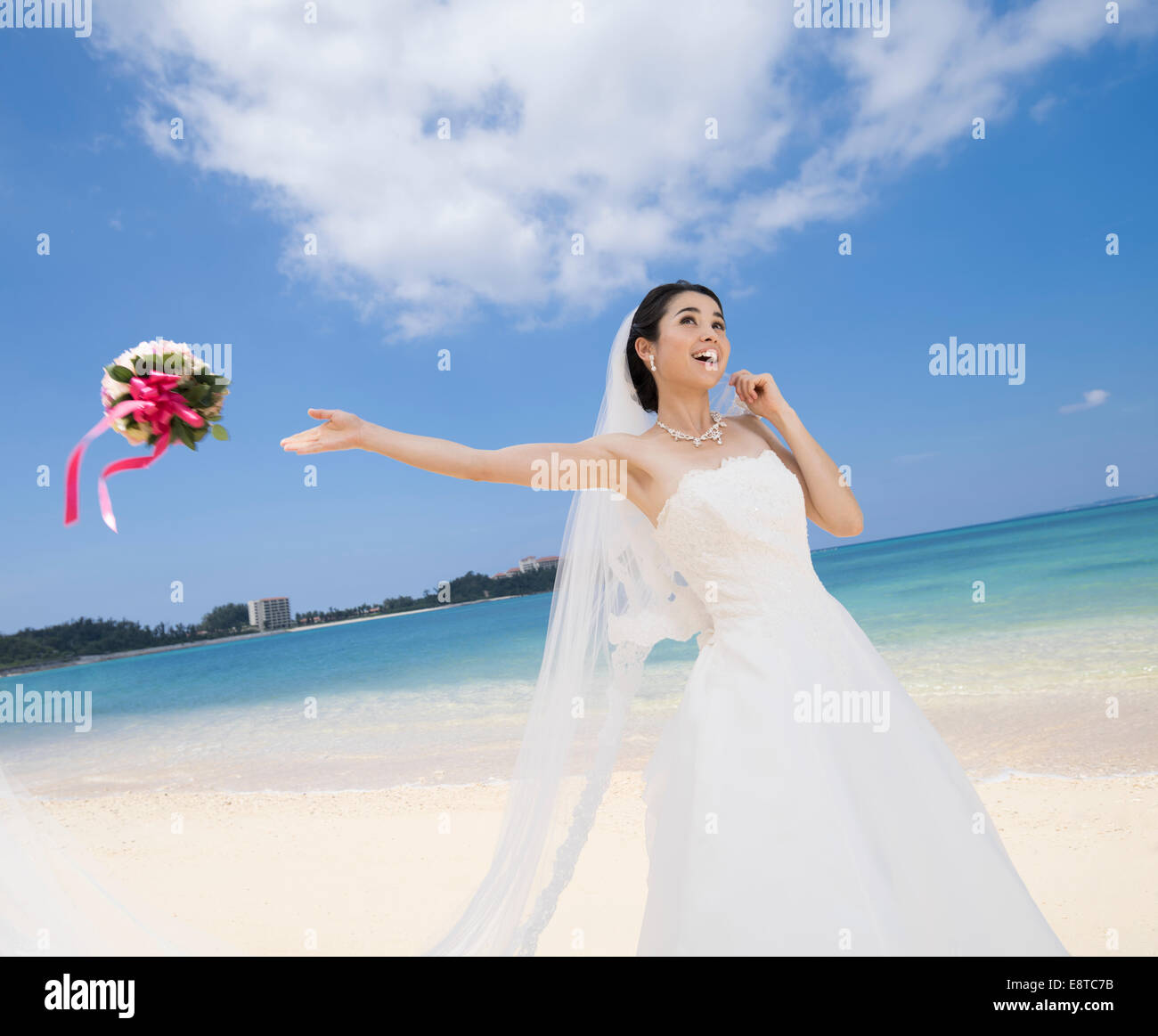 Mischlinge, asiatische / American Braut im weißen Hochzeitskleid werfen Blumenstrauß am Strandhochzeit in Okinawa, Japan Stockfoto