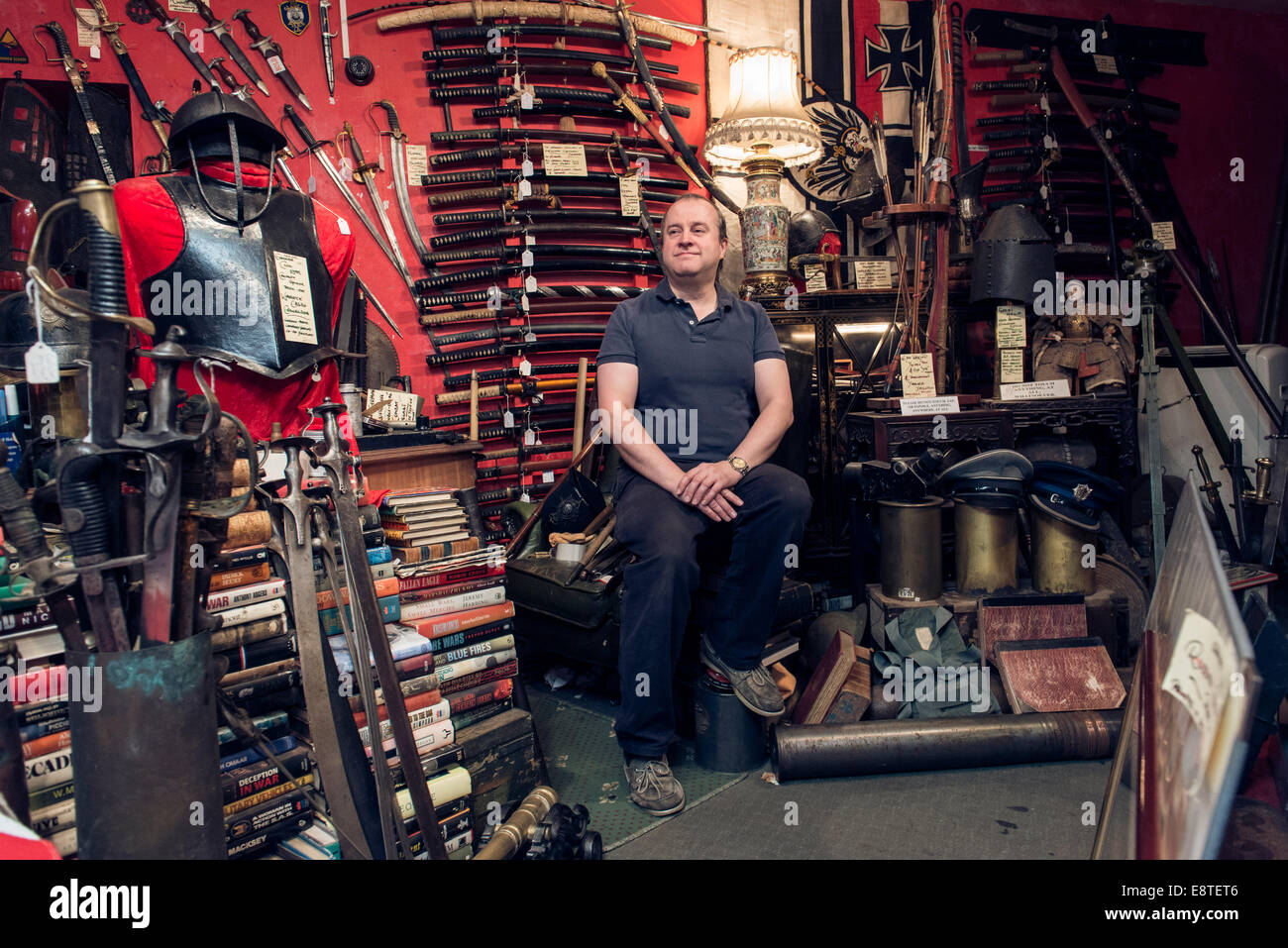 Eine männliche Krämer steht in seiner historischen militärischen Antiquitätengeschäft, umgeben von Waffen, Schwerter, Gewehre, Rüstung etc.. Stockfoto