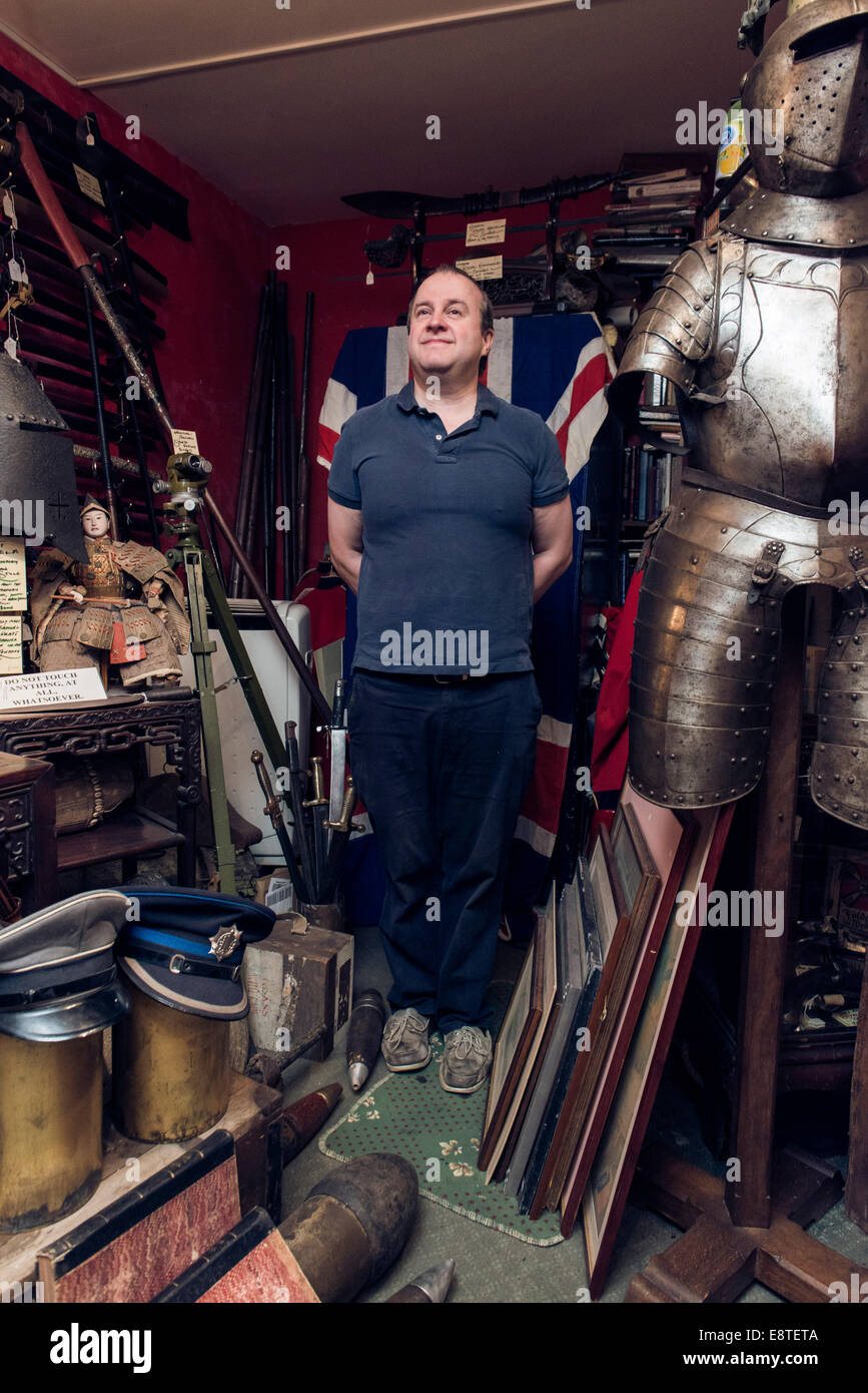 Eine männliche Krämer steht in seiner historischen militärischen Antiquitätengeschäft, umgeben von Waffen, Schwerter, Gewehre, Rüstung etc.. Stockfoto