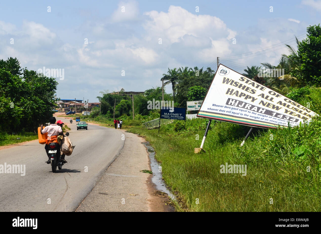 Ein Motorradfahrer, Reiten in Nigeria, Westafrika, Bundesstaat Osun, vorbei an einem Schild frohes neues Jahr an Muslime (Hijrah 1434) Stockfoto