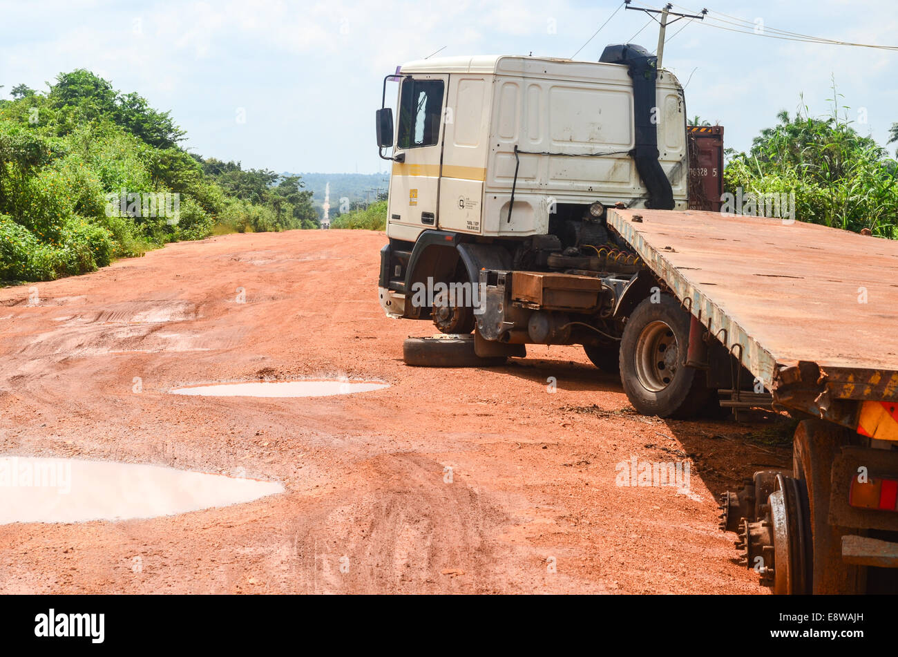 Schlammige Feldwege in Nigeria während der regnerischen Jahreszeit und einem zerstörten Lastwagen mitten auf der Straße Stockfoto
