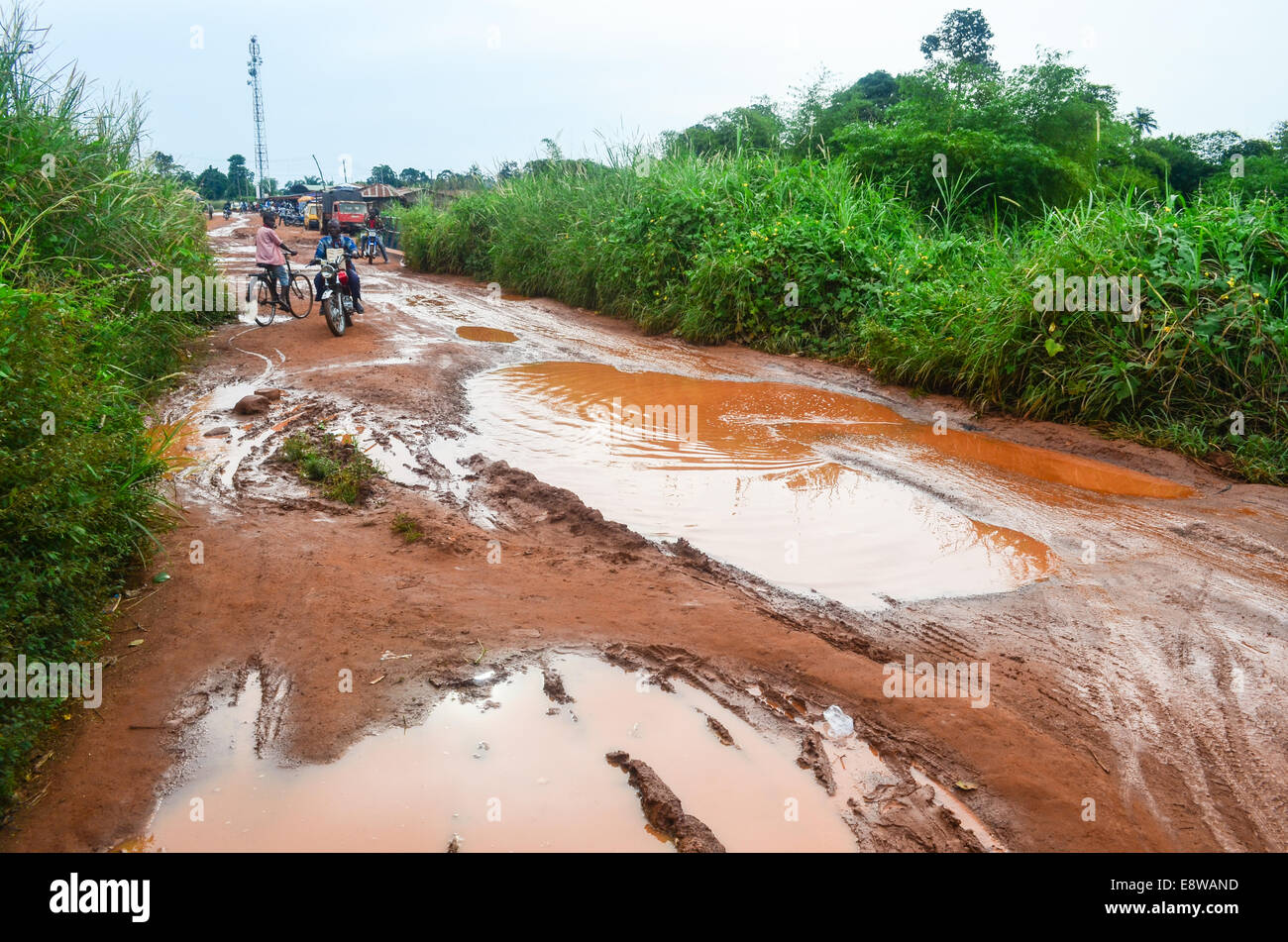 Schlammige Feldwege in Nigeria während der Regenzeit mit Motorradfahrer versucht, zwischen den überfluteten Pfützen zu navigieren Stockfoto