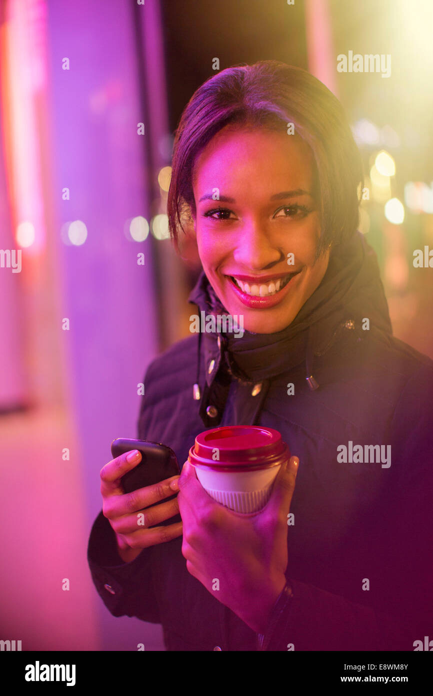 Frau auf der Stadtstraße mit Kaffee und Handy in der Nacht Stockfoto