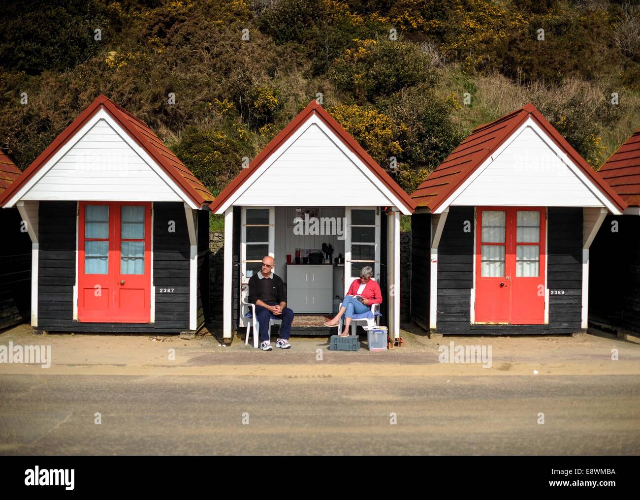 Ein paar sind zu sehen, entspannen in der Sonne neben ihre Strandhütte neben Meer in Bournemouth Stockfoto