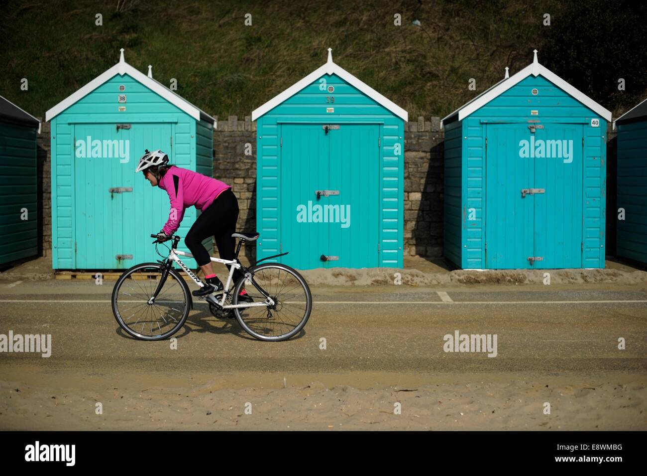 Eine Frau sieht man Radfahren vorbei an einer Reihe von Strandhütten direkt am Strand in Bournemouth, England Stockfoto