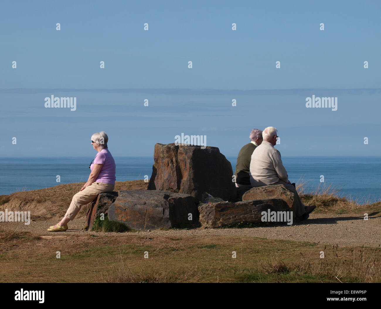 Menschen saßen auf einer öffentlichen Bank hergestellt aus großen Steinen entlang der südwestlichen Küstenweg Widemouth Bay, Bude, Cornwall, UK Stockfoto