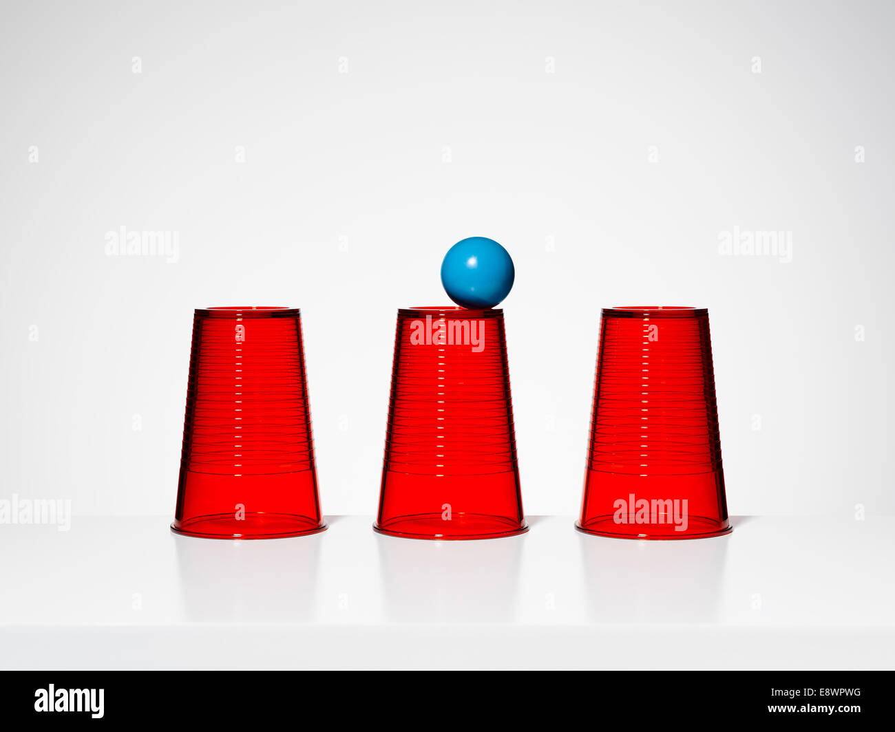 Blaue Kugel balancieren auf mittleren von drei roten Tassen Stockfoto