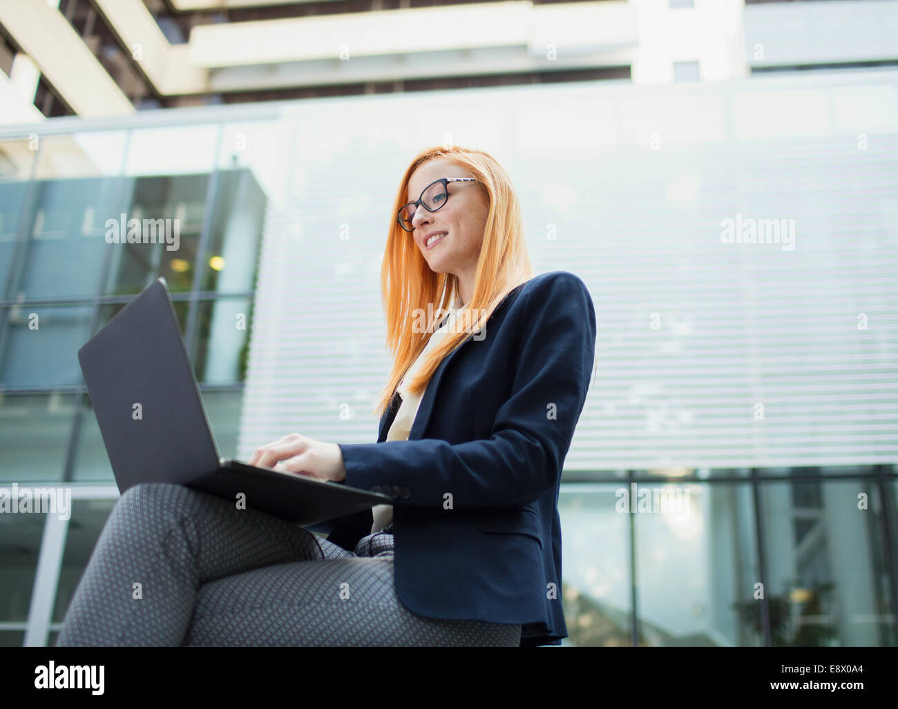 Geschäftsfrau, die Arbeiten am Laptop vor Bürogebäude Stockfoto