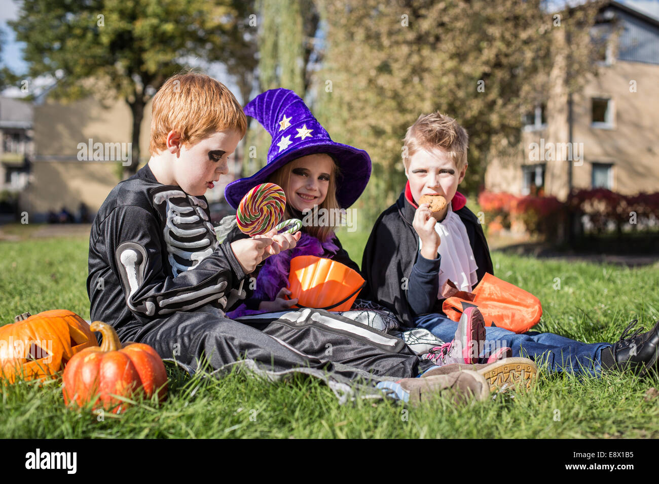 Drei kleinen niedlichen Freunde sitzen auf dem Rasen und Halloween-Süßigkeiten essen Stockfoto