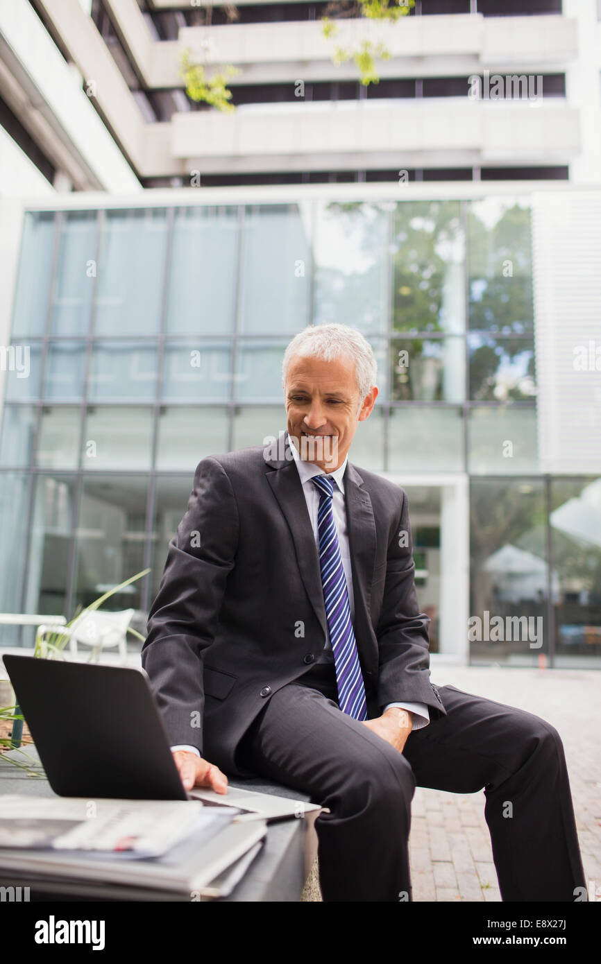 Geschäftsmann mit Laptop auf Bank außerhalb Bürogebäude Stockfoto