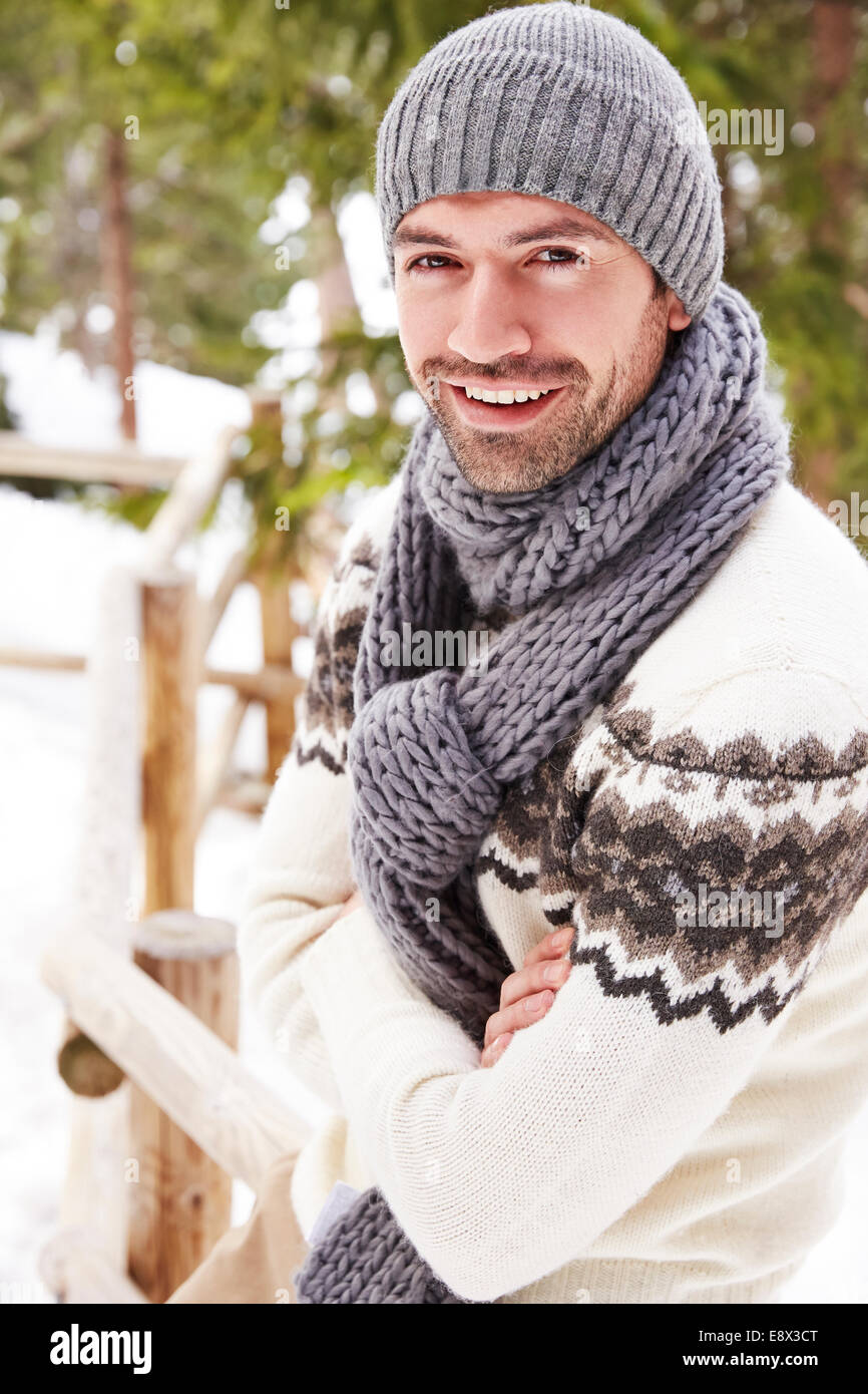 Lächelnder Mann sitzt auf verschneiter Zaun Stockfoto