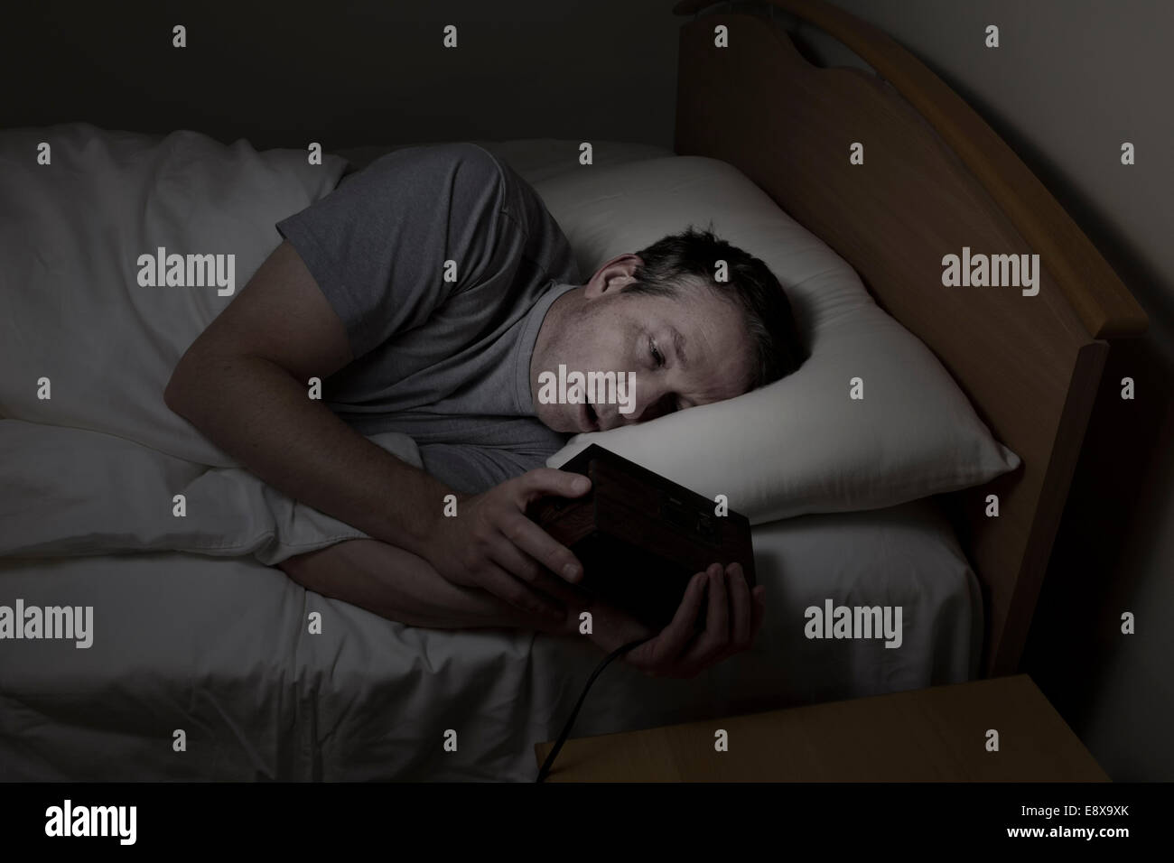 Reifer Mann, Augen mit beiden Händen auf Wecker während der Überprüfung Zeit öffnen, kann nicht schlafen in der Nacht unter Schlaflosigkeit Stockfoto