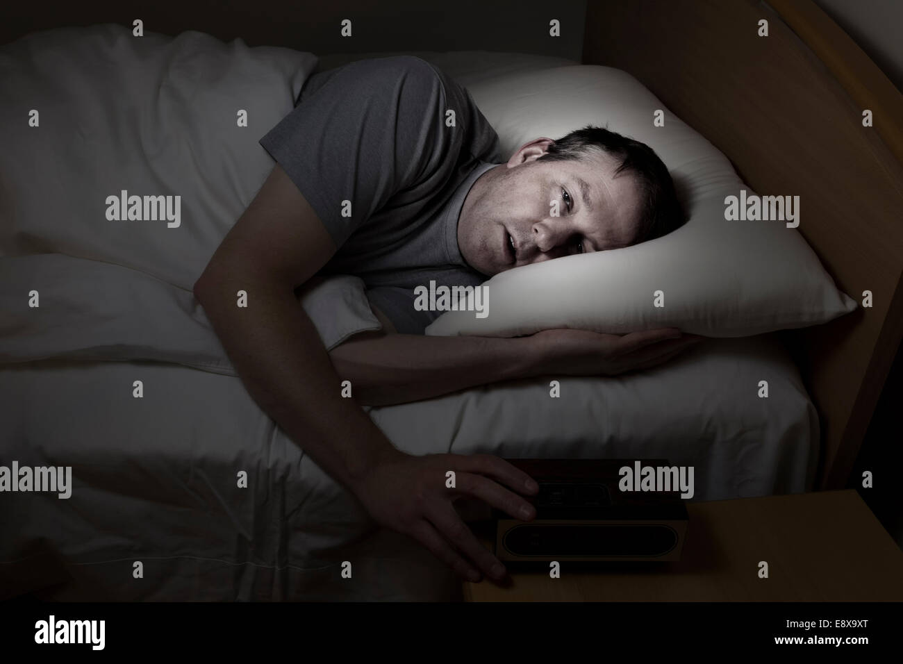 Reifer Mann, Augen weit offen mit Hand am Wecker, kann nicht schlafen in der Nacht unter Schlaflosigkeit Stockfoto