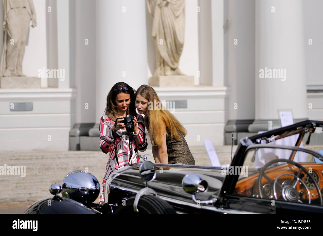Zwei Frauen, steht man vor einem Oldtimer, schauen Sie sich das Bild, das man von ihnen nur auf der Kamera genommen hat, die sie hält Stockfoto