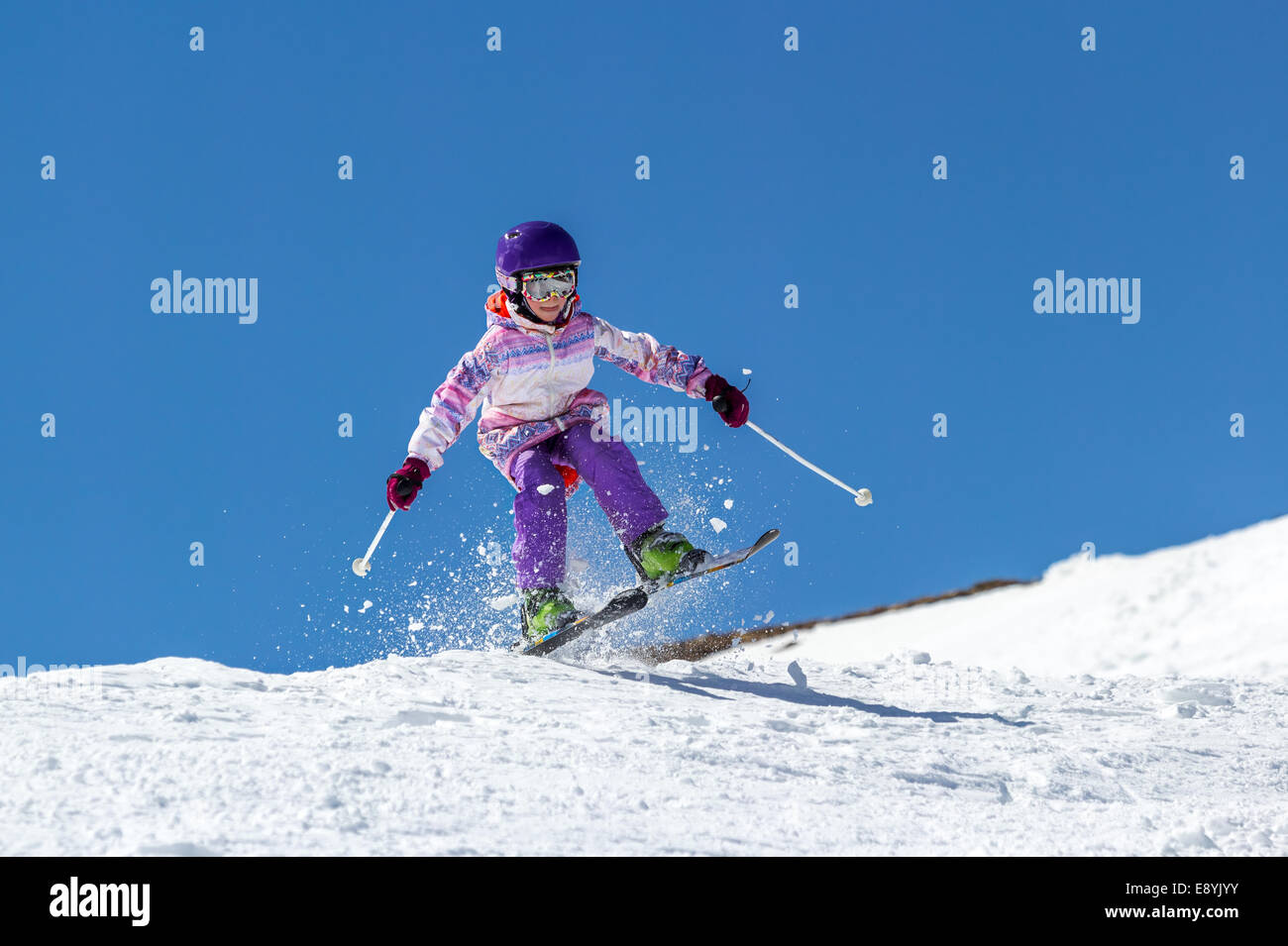 Kleine Mädchen Skifahrer steigt über einen Hang in einen Sprung auf einem Hintergrund von klaren Himmel Stockfoto