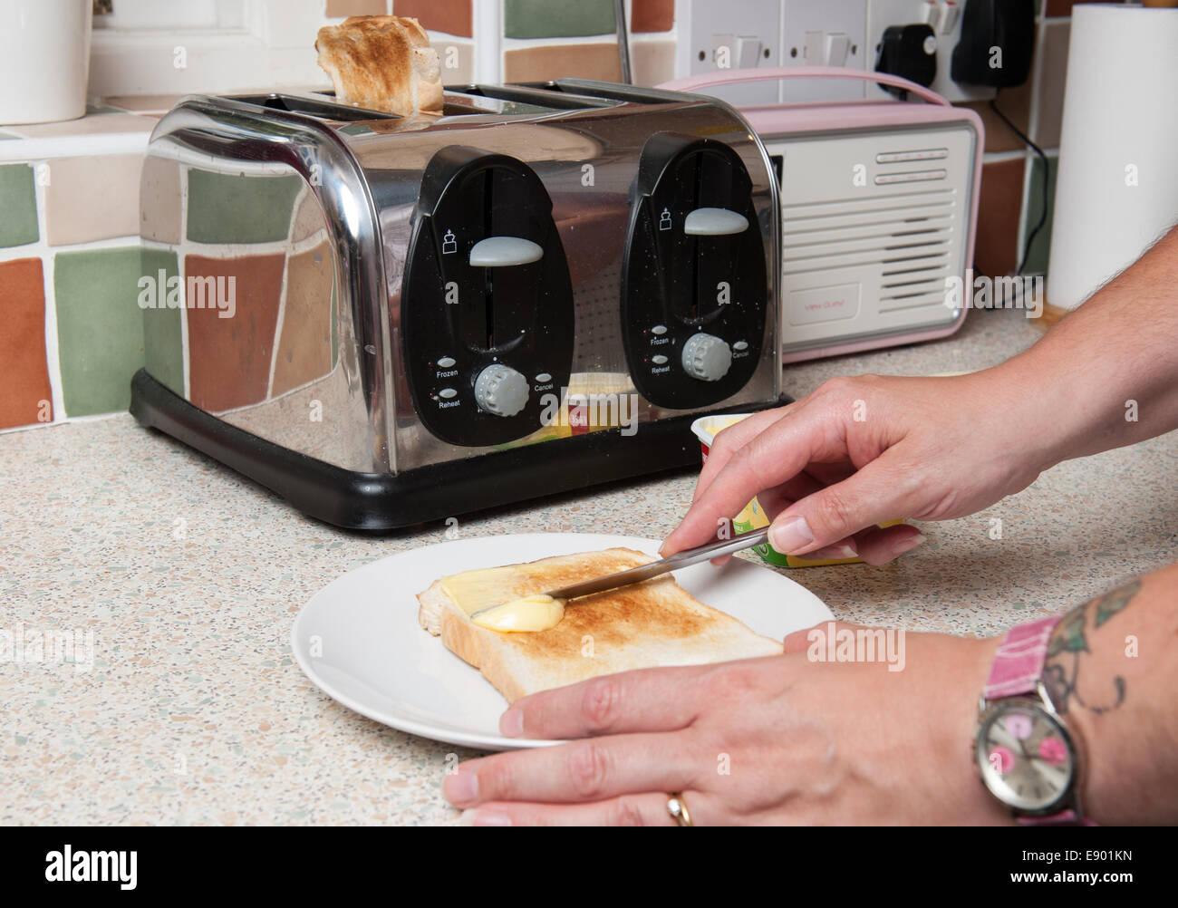 Mann eine Scheibe Toast in einer Küche mit den Toaster im Hintergrund schmieren Stockfoto