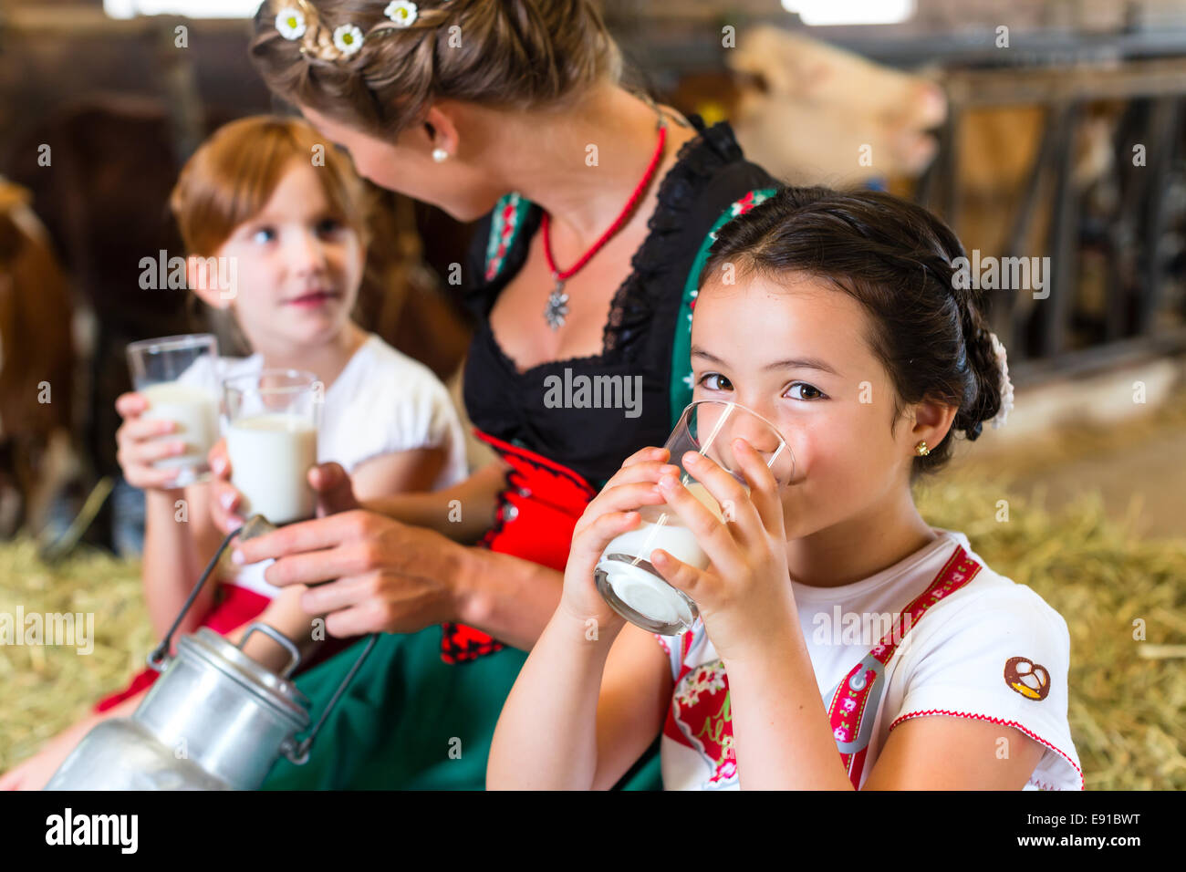 Bayerin sitzen mit Kinder im Kuhstall auf Heuballen trinken frischen Milch Stockfoto