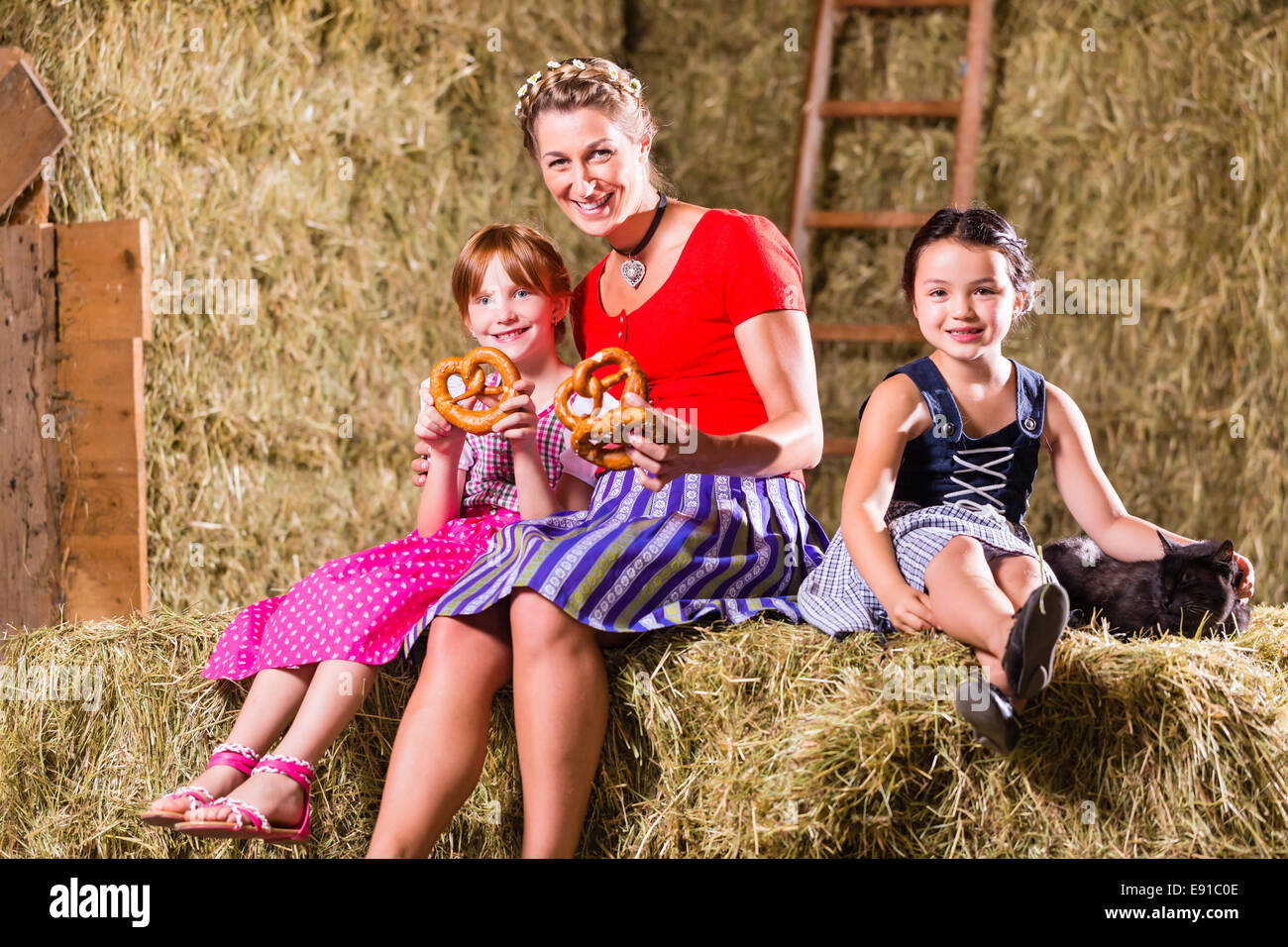 Bayerische Mutter und Kinder sitzen auf dem Heuboden mit Brezeln Stockfoto