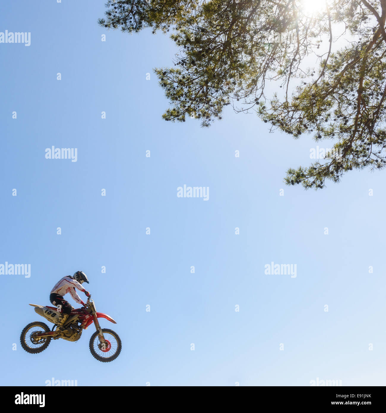 Dirt-Biker springt hoch in der Luft gegen einen blauen Himmel und die Baumkrone Stockfoto