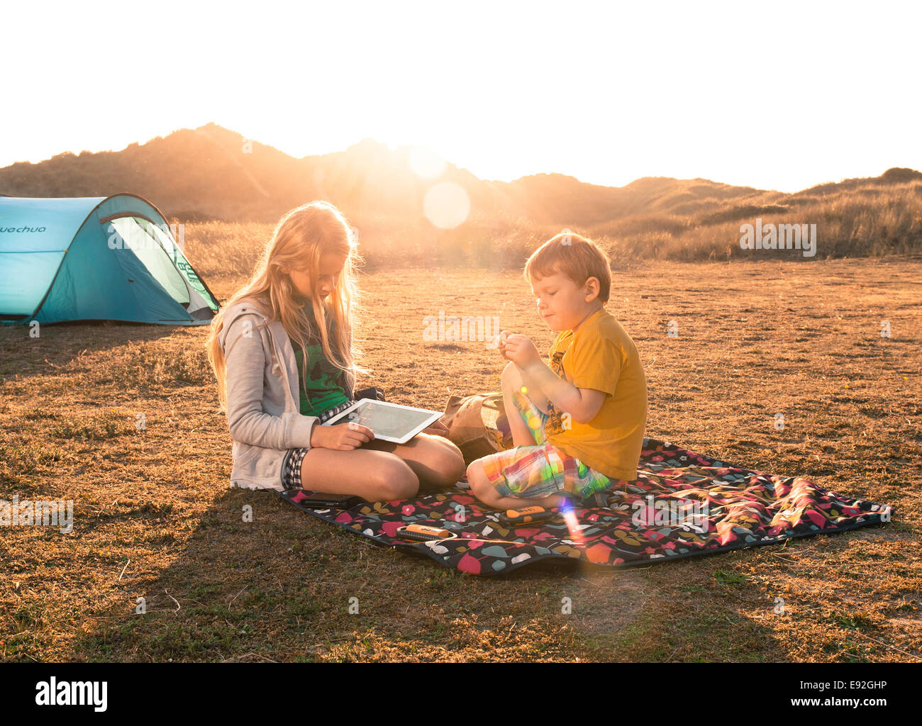 Kinder camping auf der Picknickdecke mit dem Ipad im Sommer. Bruder und Schwester camp Urlaub in UK England Sanddünen Stockfoto
