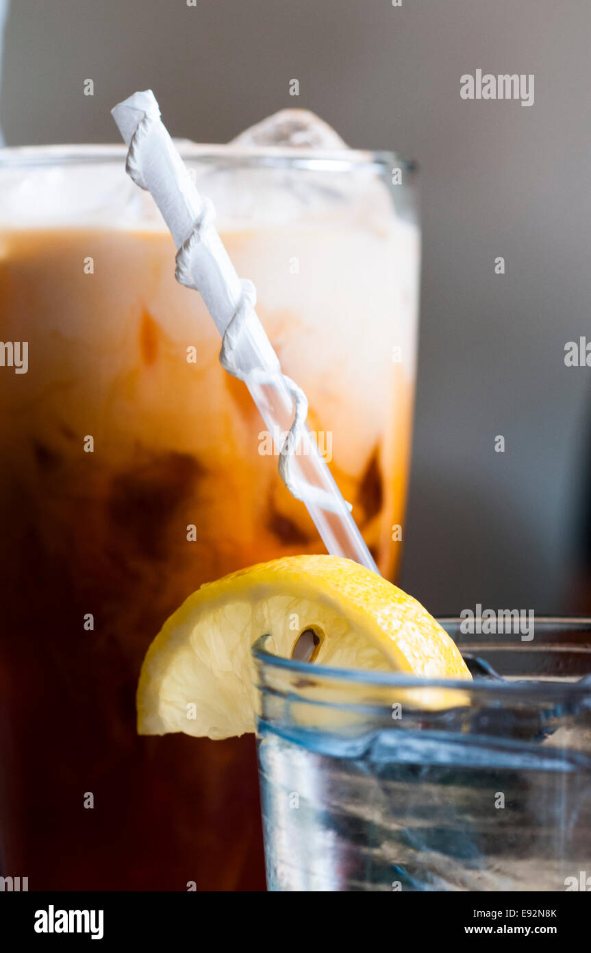 Glas Wasser mit Stroh und Zitrone Scheibe mit Eiskaffee im Hintergrund Stockfoto
