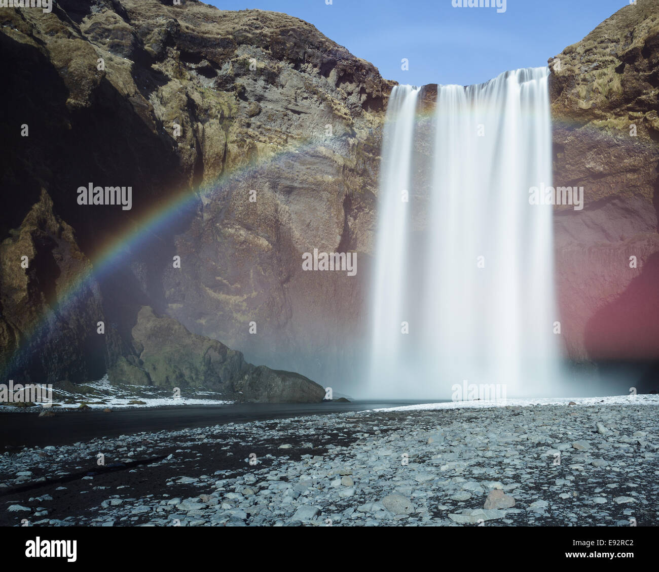Skógafoss Wasserfall Island steinige Ufer blauen Himmel Regenbogen Stockfoto