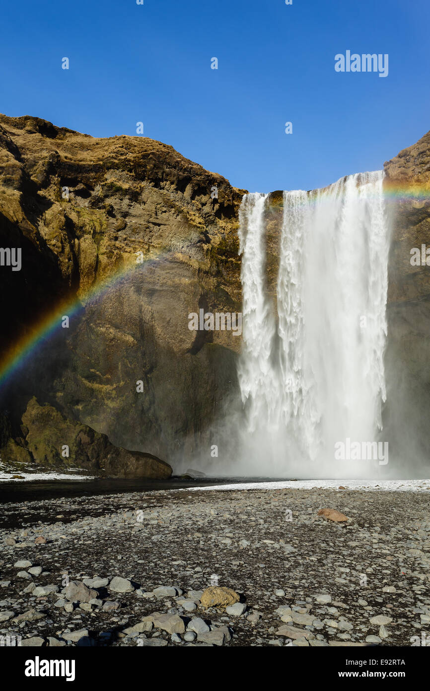Skógafoss Wasserfall Island Rainbow steinige Ufer blauer Himmel Stockfoto