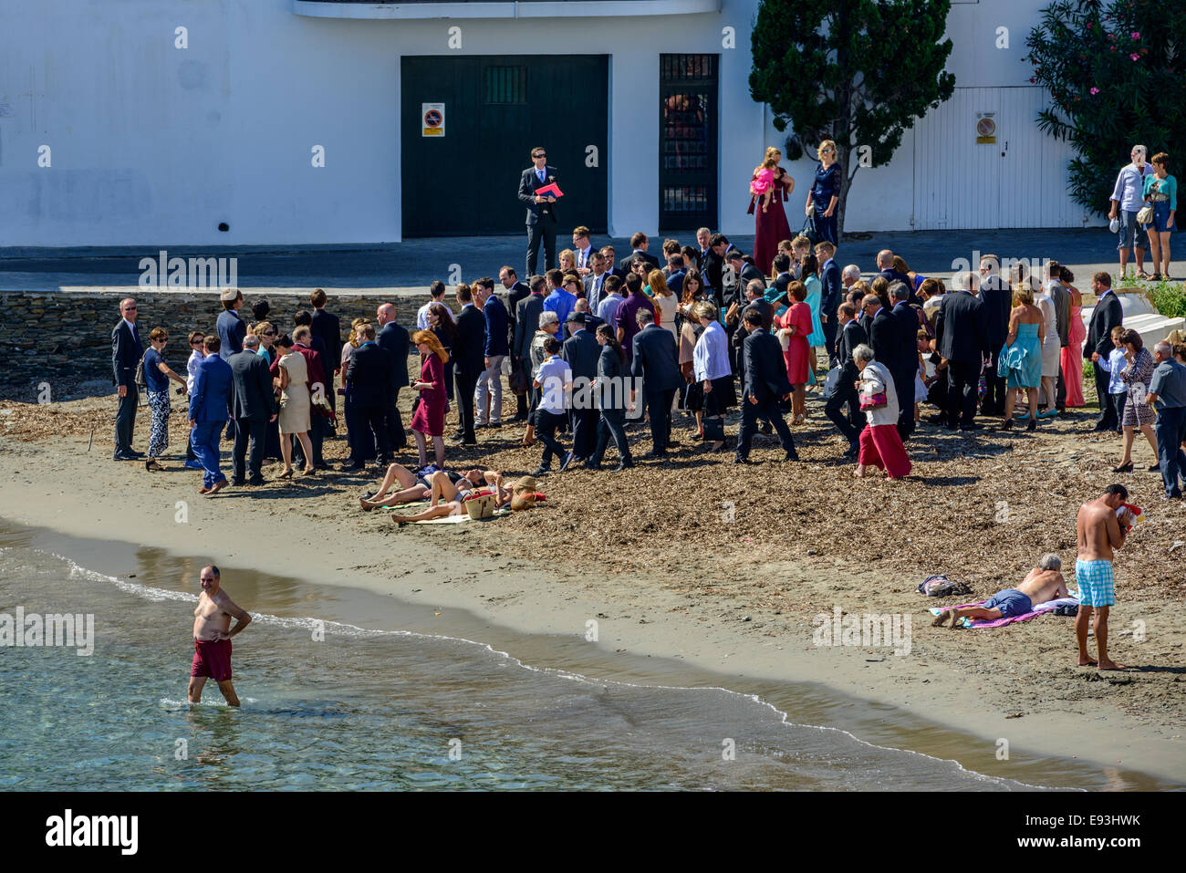 Eine Hochzeitsfeier sammelt für ein Gruppenfoto am Strand, unter eine neugierige Schar von Strandurlauber in schwimmen Kleidung. Stockfoto