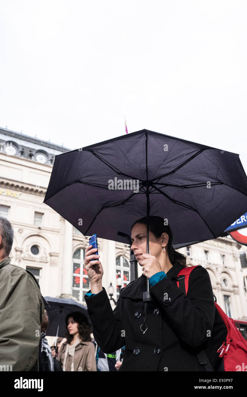 Eine Frau unter einem Regenschirm im Regen Lesen ihres Mobiltelefons Abschirmung Stockfoto