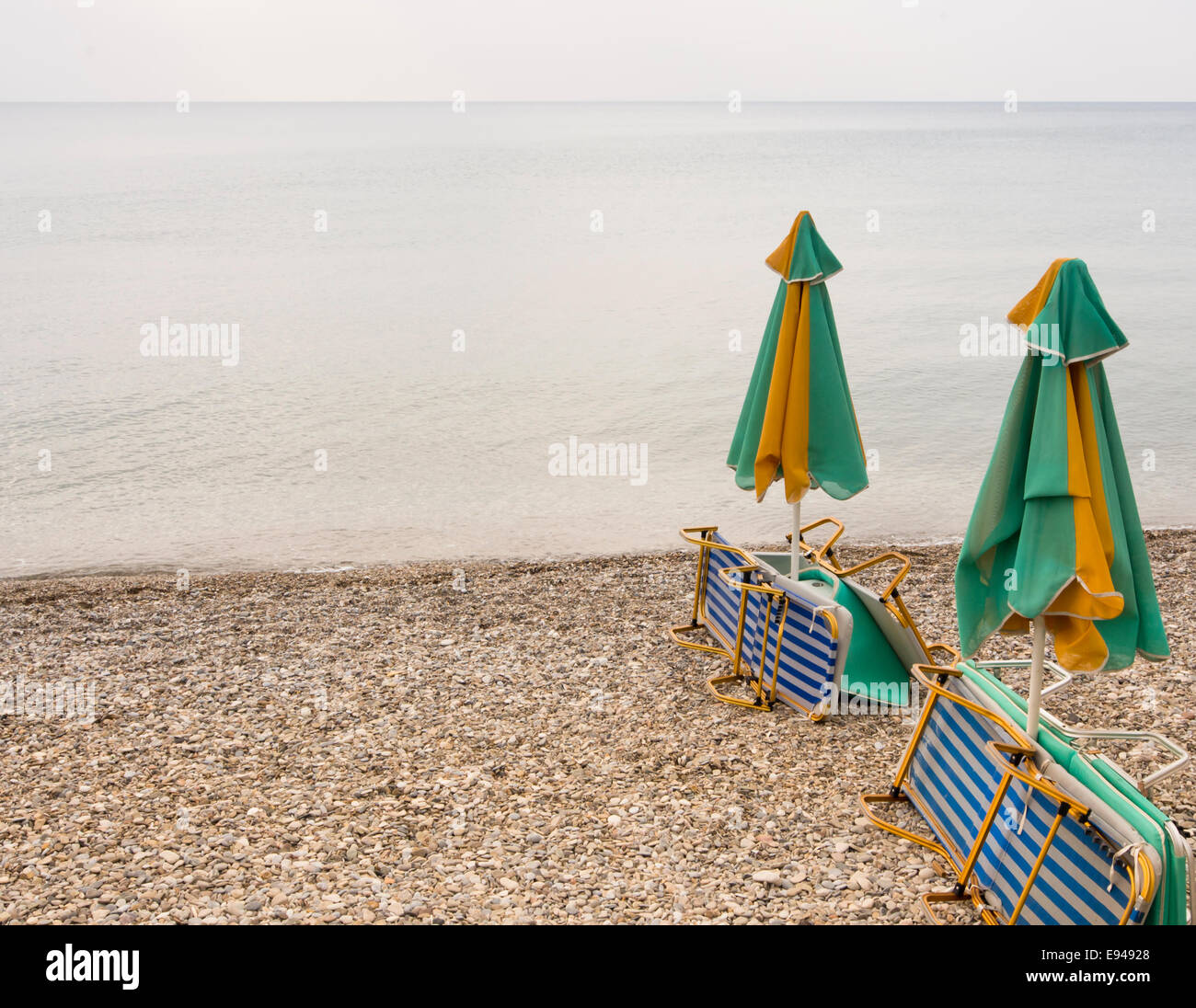 Düster Tag am Strand, Sonnenliegen, geschlossene Sonnenschirme, grauen Himmel leer niemand spielen im Wasser oder mit Kieselsteinen, Samos Griechenland Stockfoto