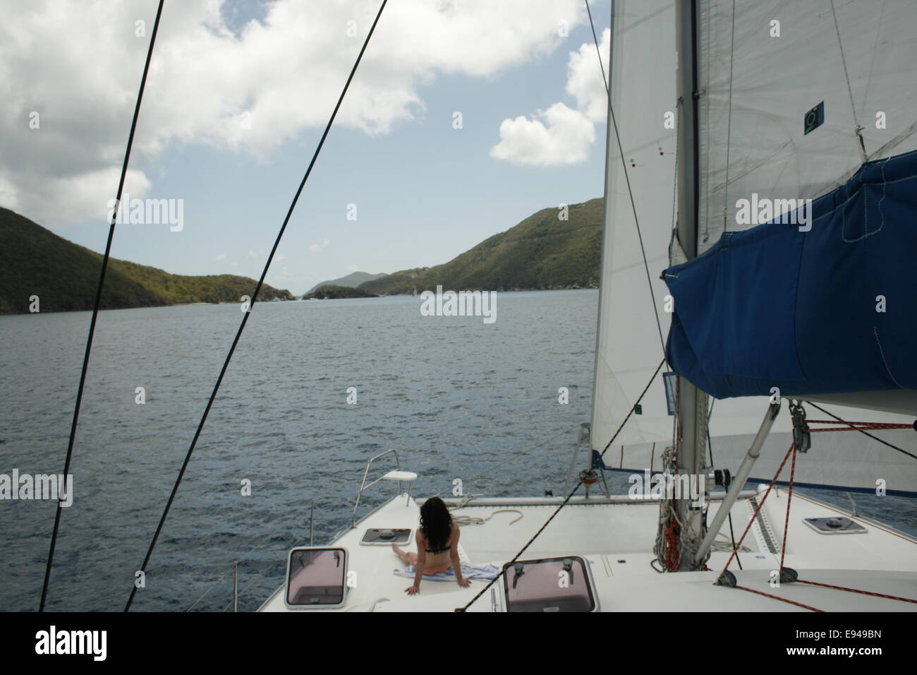 Eine junge Frau sitzt auf dem Deck eines großen Katamarans im Urlaub auf den BVI. Stockfoto