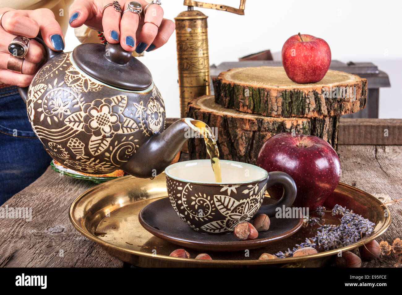 Frau, Gießen Tee von Teekanne auf Vintage Holztisch mit Haselnüssen Äpfel und goldenen Kaffeemühle im traditionellen Stil Stockfoto