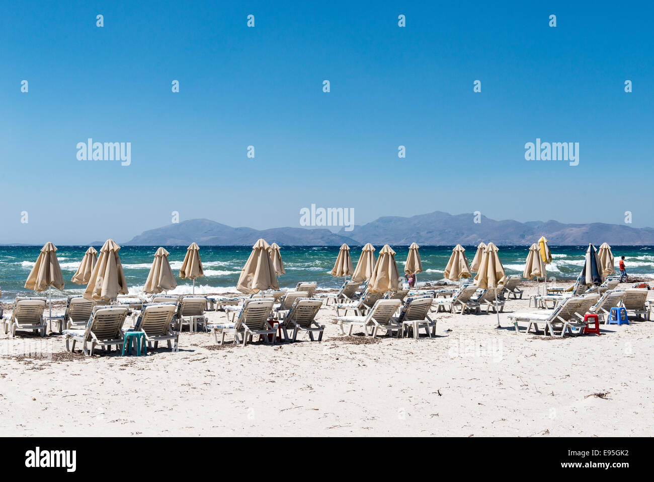 Leeren Strand mit geschlossenen Sonnenschirme und Liegestühle am Strand von Mastichari, Insel Kos, Griechenland Stockfoto