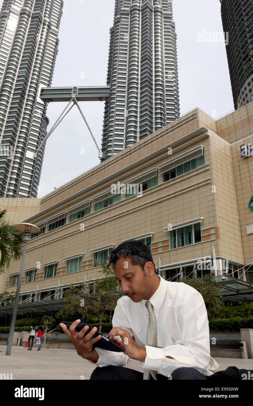 Junger Mann mit Tablet sitzend auf Straßenseite vor Kualalumbur Twin tower Stockfoto