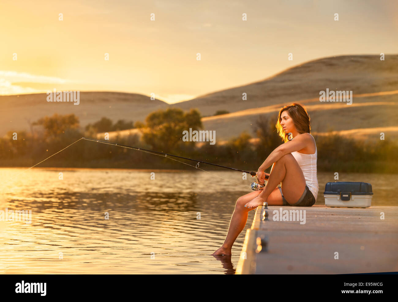 Junge Frau Angeln von einem Dock an einem kleinen See bei Sonnenuntergang. Stockfoto
