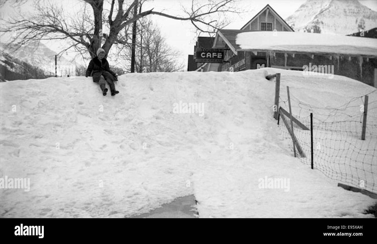 Foto eines Kindes, das in den 1940er oder 1950er Jahren auf einer Straße in Fort Macleod, Alberta, eine Schneebank hinunterrutscht Das Foto ist Teil eines Albums, das das Leben in der Region Mitte des 20. Jahrhunderts dokumentiert. Stockfoto