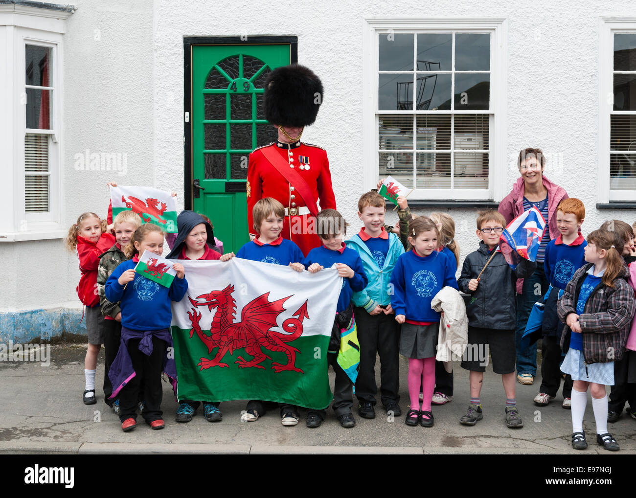 Ein Offizier der Walisischen Garde mit einigen Kindern der Presteigne-Grundschule mit walisischer Flagge (Powys, Wales, Vereinigtes Königreich) Stockfoto