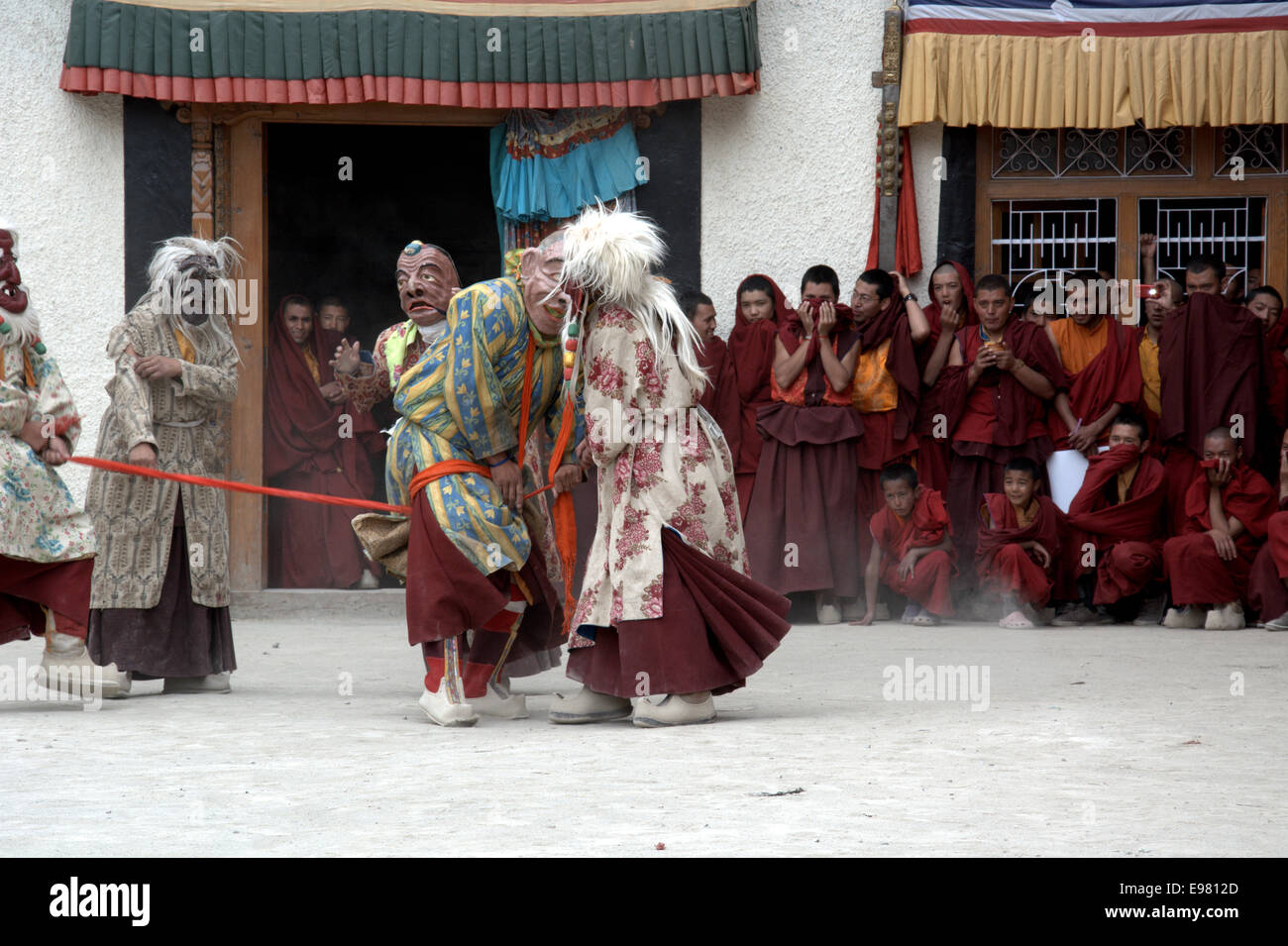 Maskierte Darsteller inszenieren den theatralischen Teil eines Cham-Tanzrituals, das von aufmerksamen buddhistischen Mönchen in einem Ladakhi-Kloster beobachtet wird. Stockfoto