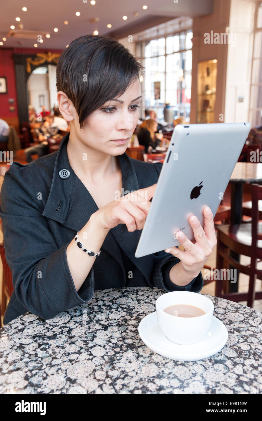 Junge Frau, die das Surfen im Internet auf ein Apple iPad Tablet-Computer mit gratis Kaffee Shop wi Fi, London, England, UK Stockfoto