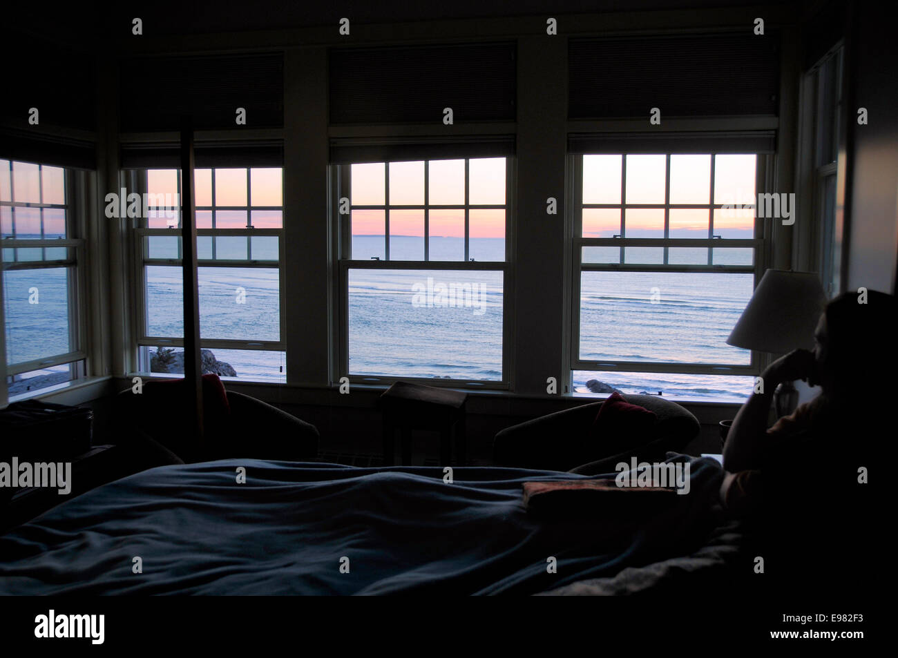 Frauen im Schatten sitzend im Bett 4 Fenster mit Blick auf den Sonnenaufgang. Strände farbig orange Ozean Himmel füllt Windows. Stockfoto