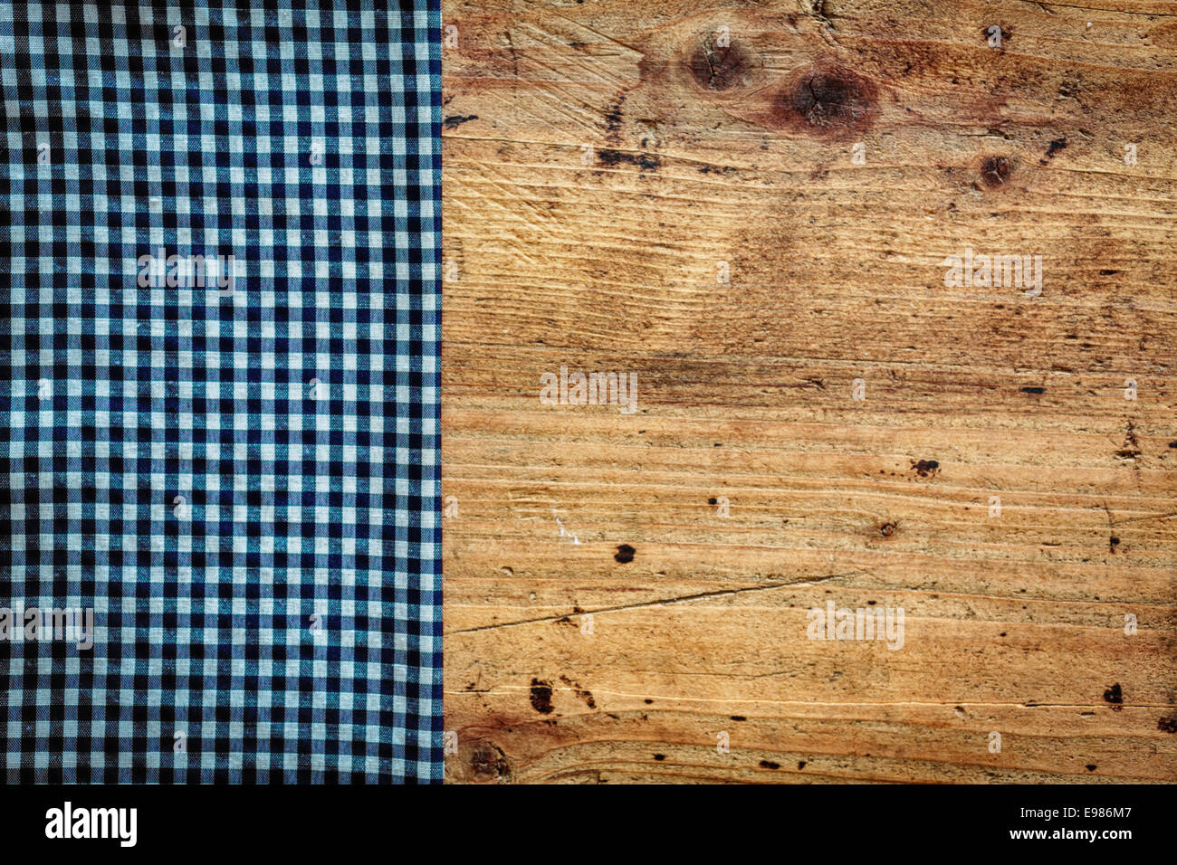 Konzeptbild von einem Land Küche Hintergrund mit einer alten gebeiztem Holz Oberfläche überlagert durch eine frische blaue und weiße gefaltete Serviette als Grenze auf der linken Seite Stockfoto