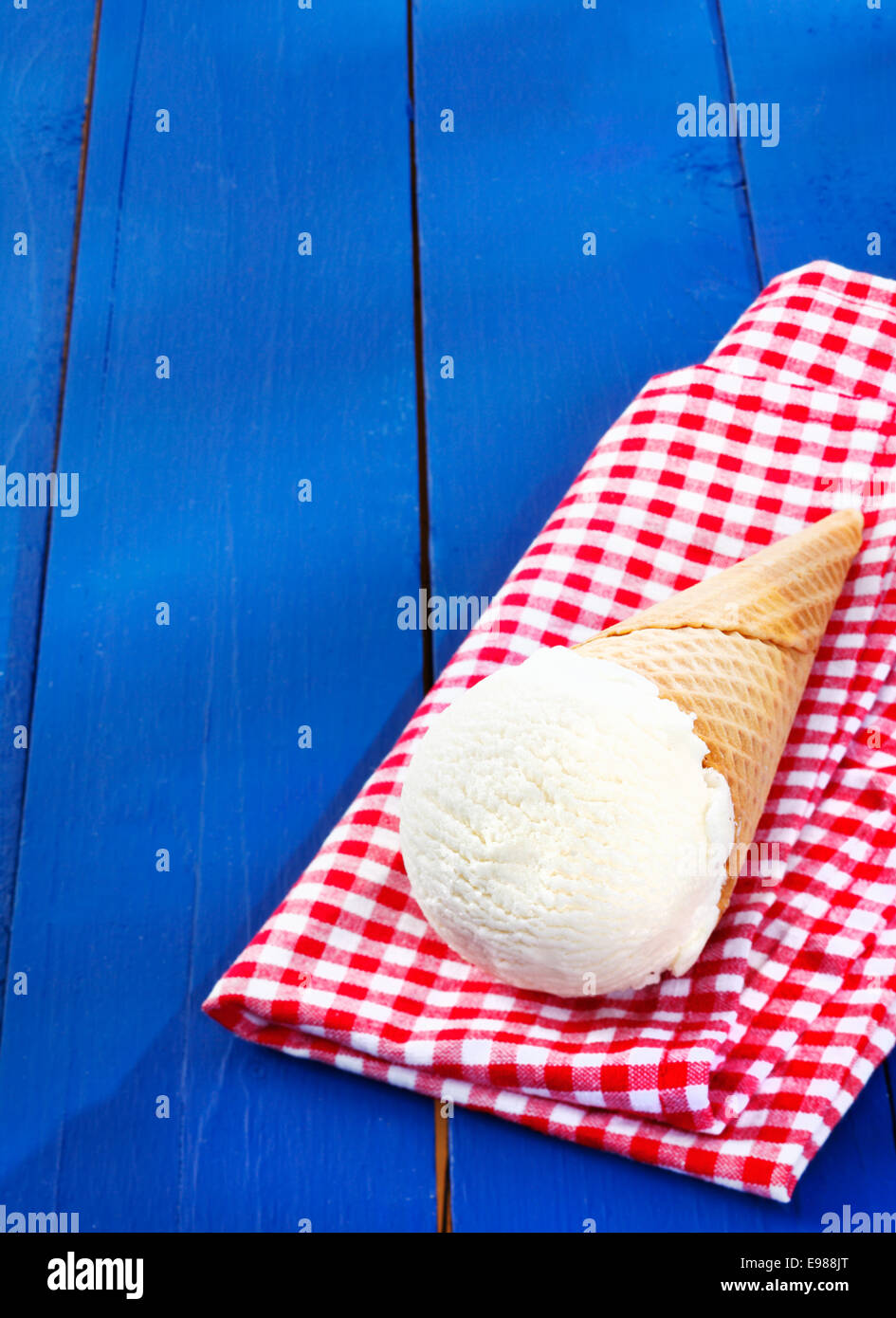 Vanille Eis serviert in einem Kegel auf einer bunten rot-weiß karierte Serviette auf urigen Holzbrettern mit Exemplar Stockfoto