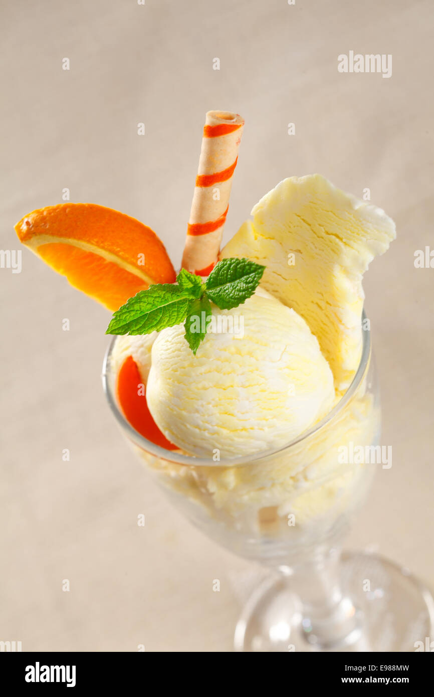 Cremige tropische Eis Dessert mit süß Orangenscheiben und einem bunt gestreiften Wafer Keks Stockfoto