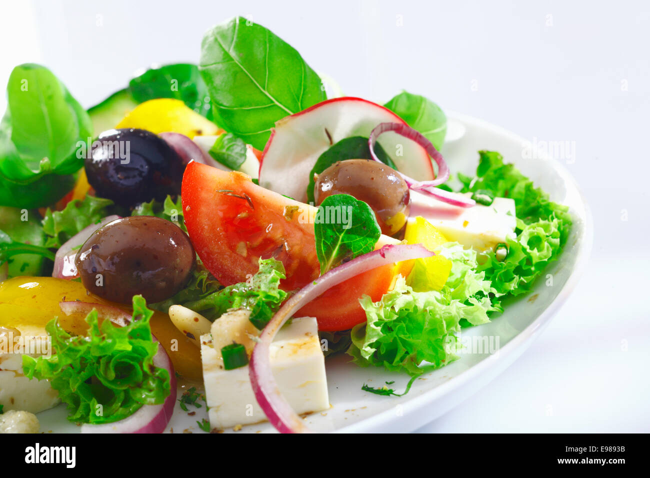 Detailansicht einer Portion knackige appetitlich griechischer Salat mit Kopfsalat, Basilikum, Schafskäse, Zwiebeln, Oliven, Radieschen und Tomaten Stockfoto