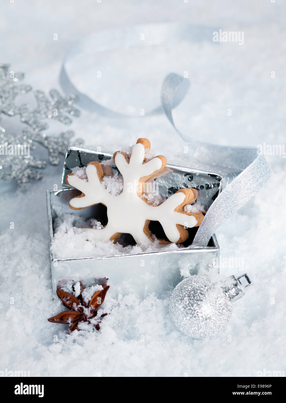 Christmas iced Schneeflocke Keks in einer Geschenkbox liegen im Schnee umgeben von anderen festliche Ornamente und Sternanis Gewürz Stockfoto