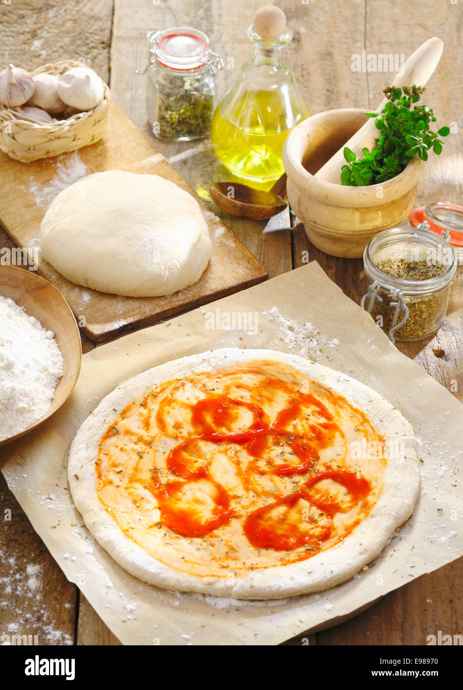 Vorbereitung eine italienische Pizza mit neu gerollt Tortekruste Basis mit Tomatenmark auf dem bemehlten Papier verteilt und umgeben von anderen Zutaten Stockfoto