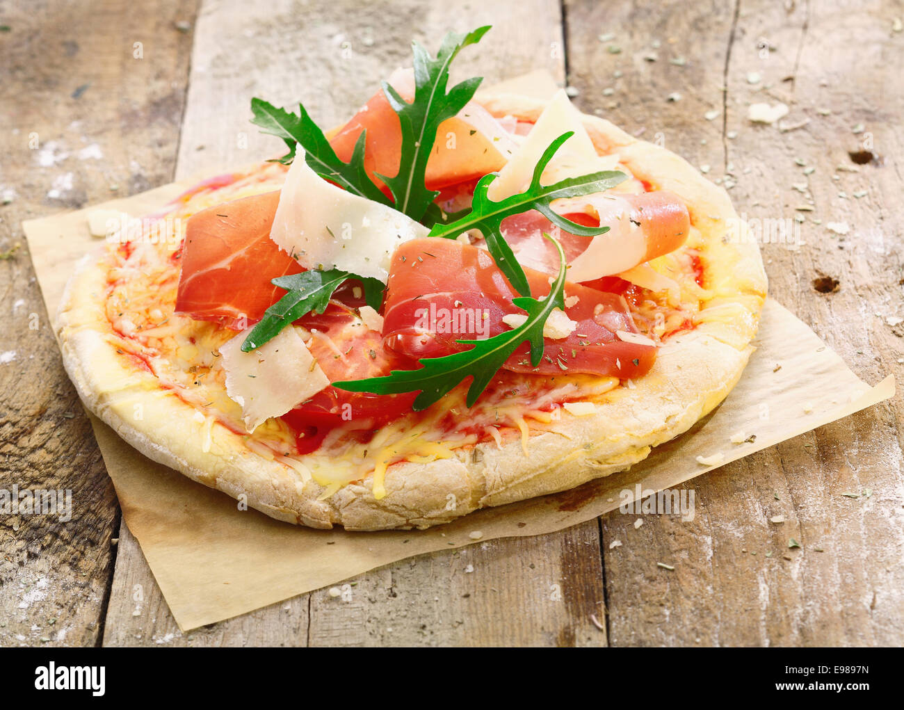 Frisch zubereitete leckere Pizza auf dem Ofen Papier mit einem goldenen Sockel mit leckeren Schinken, Käse, Tomaten und frischen grünen Kräutern garniert Stockfoto
