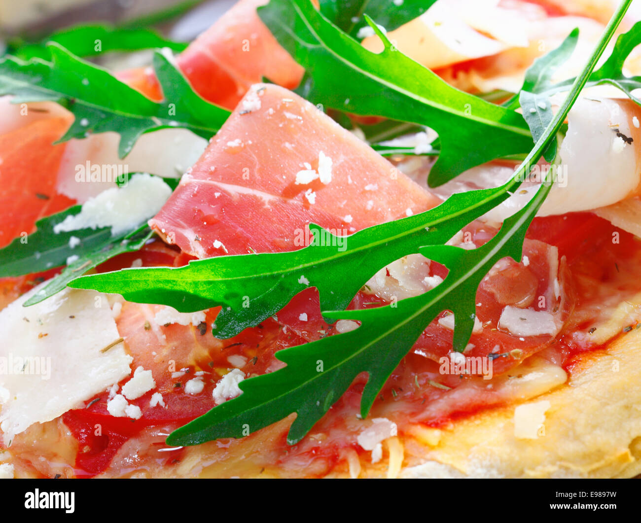 Nahaufnahme von köstlichen frischen Zutaten als Topping für italienische Pizza mit dünn geschnittenen Schinken, Tomaten, frische Kräuter, Rucola und Käse Stockfoto