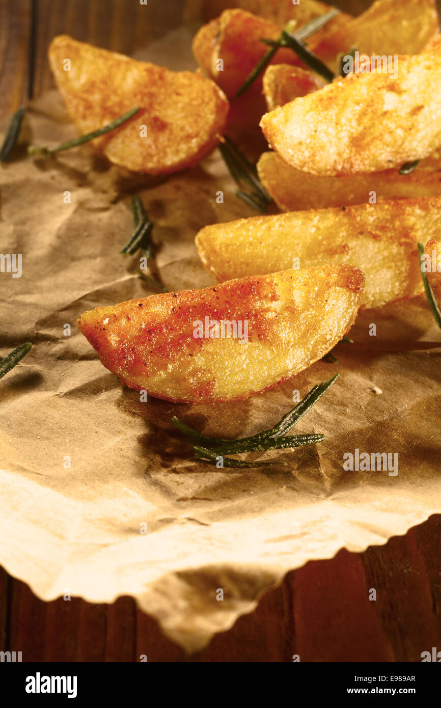 Goldene gebackene oder Gebratene Kartoffel wedges mit einer würzigen Beschichtung diente als ein Imbiss auf braunem Papier mit frischem Rosmarin Blätter Stockfoto